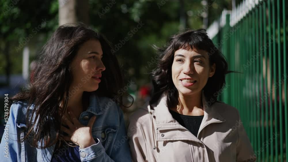 Two happy female friends laughing and smiling while in conversation walking outside in city street Two happy female friends laughing and smiling while in conversation walking outside in city street