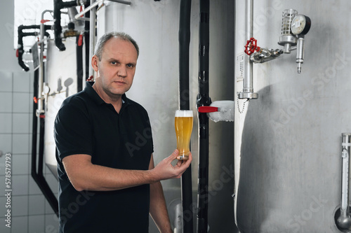 brewer at brewery checks the quality with a glass of fresh beer