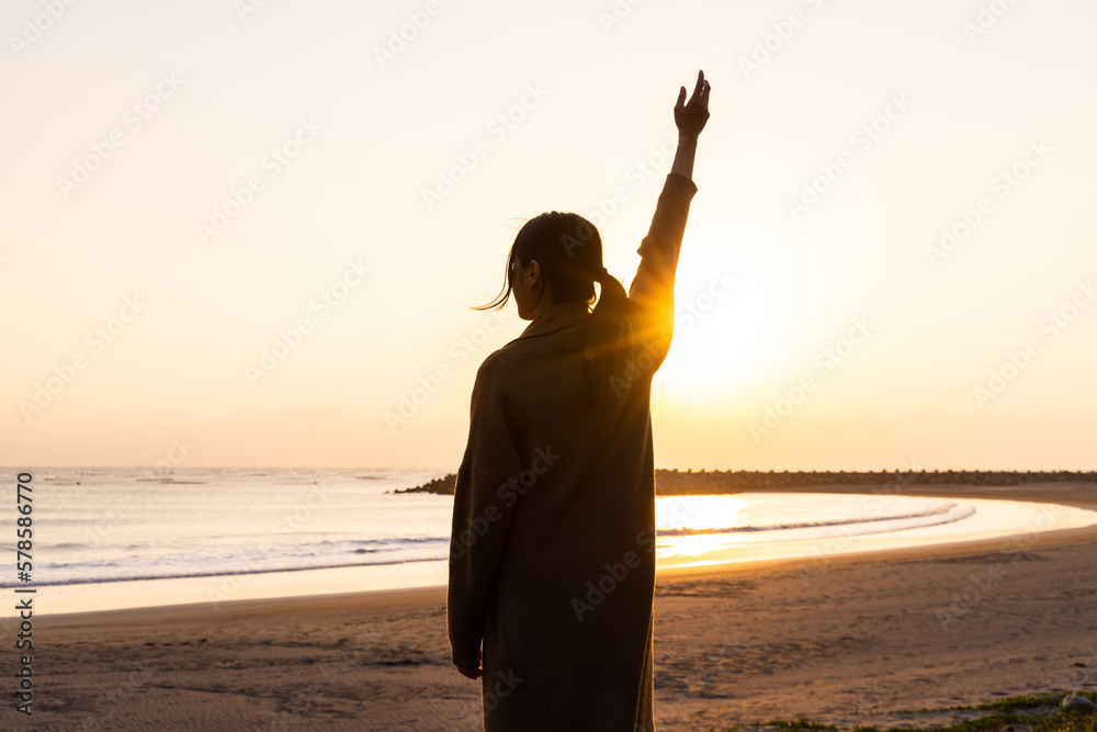 Fototapeta premium Silhouette of woman rise up the hand at sunset in the beach