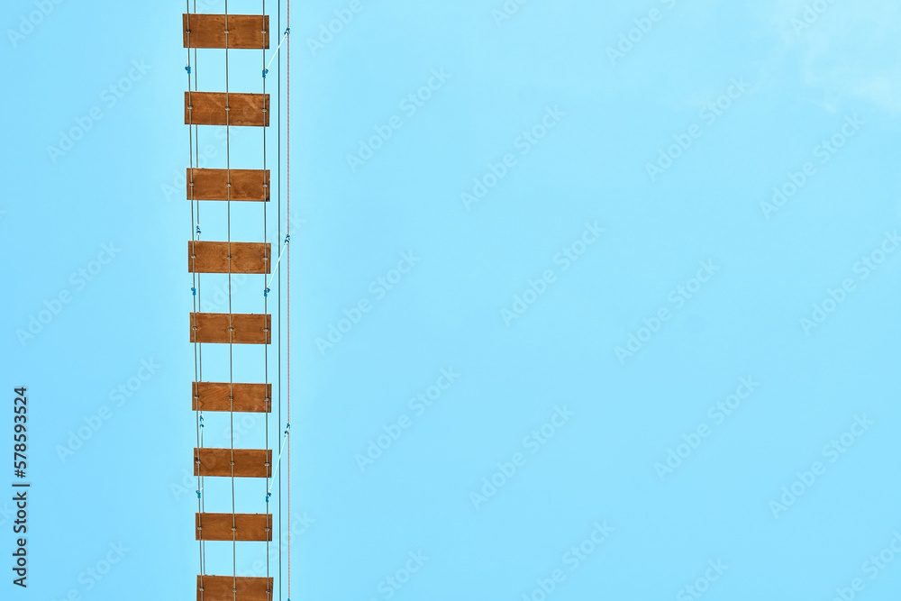 Long rope bridge with wooden planks against clear blue sky. Fun attraction for tourists in recreational water park at summer resort Long rope bridge with wooden planks against clear blue sky. Fun attraction for tourists in recreational water park at summer resort