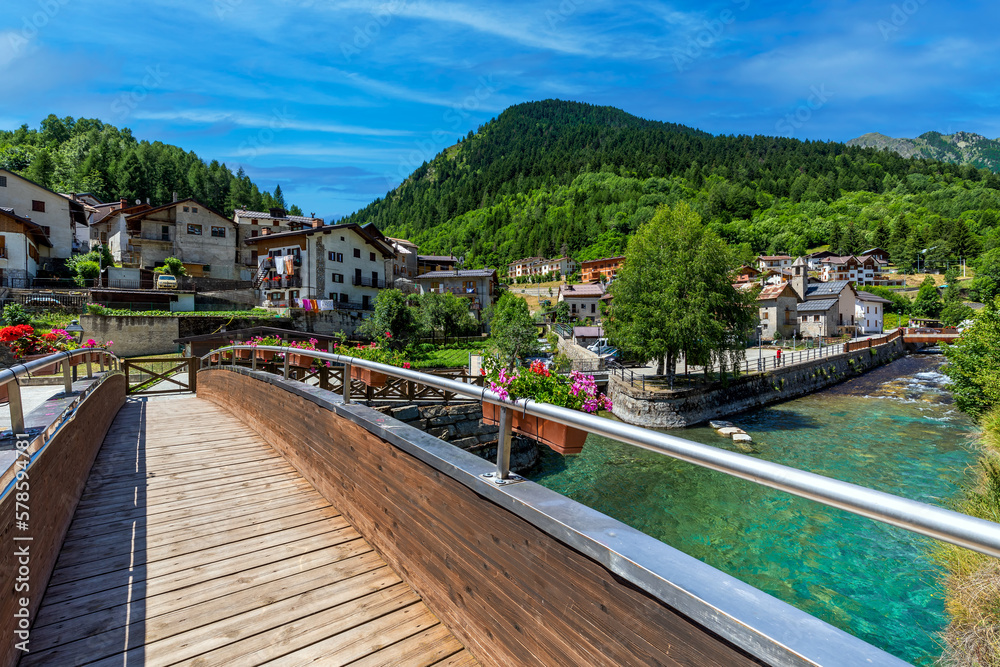 Wooden bridge over alpine creek and mountains on background in Northern Italy.
