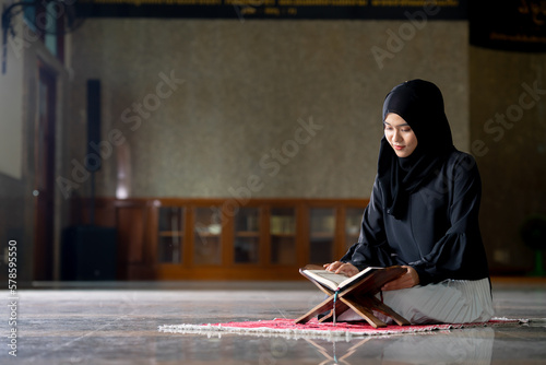 The image of an Asian Muslim woman in the Islamic religion in hijab in black color. Sitting reading the Quran and having a happy smiling face Staying in a beautiful mosque out of respect for God.