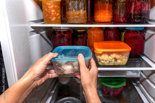 A woman puts packaged food in a home refrigerator