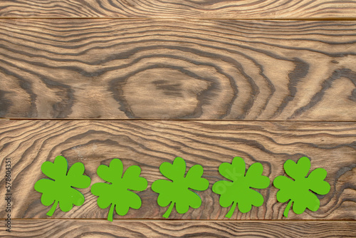 Frame of four-leaf clover and light lights. Wooden background with clover leaves. St. Patrick's Day. Textured wood, blank for holiday greetings. Flat layout. copy space.