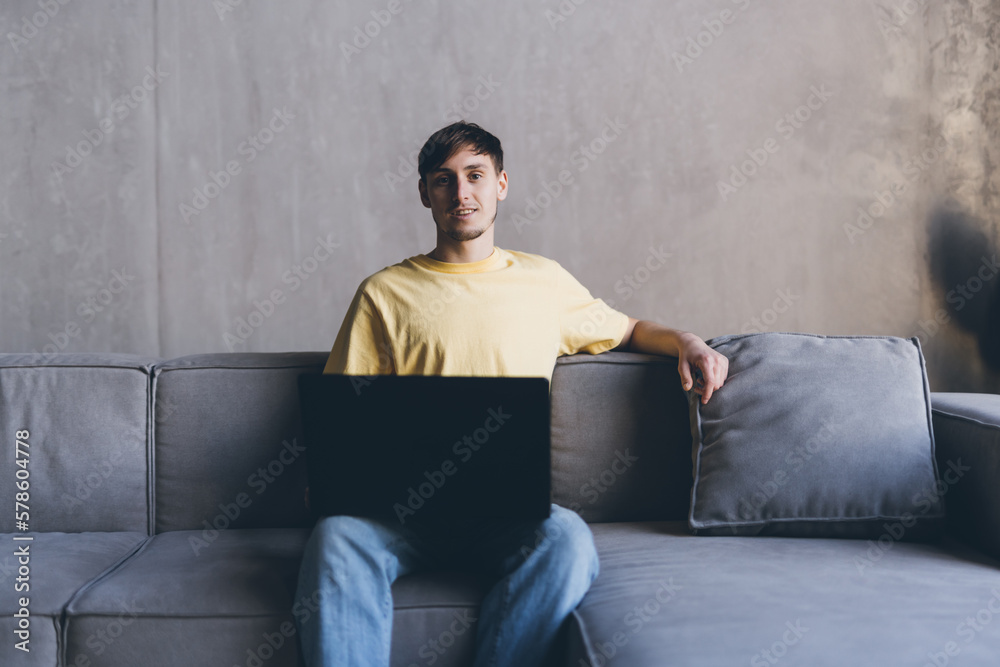 Young man sitting on a couch at home, using laptop computer