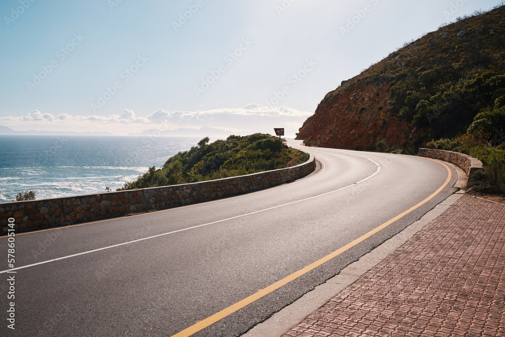Fototapeta premium Mountain, road and ocean view with no people for travel, destination or sightseeing in Cape Town. Nature, beauty on empty street for road trip, vacation or holiday on South Africa blue sky background