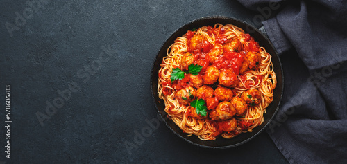 Spaghetti pasta with meatballs in tomato sauce with parsley in frying pan, dark table background, top view. Banner, copy space