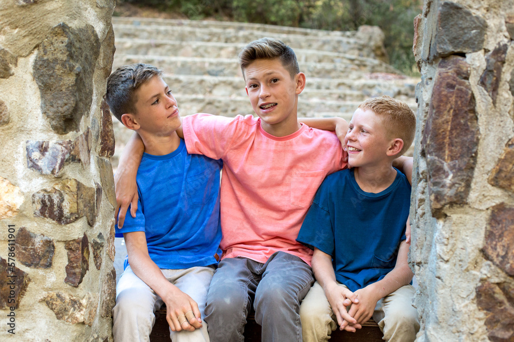 Two younger brothers look at older brother while sitting by stone wall Two younger brothers look at older brother while sitting by stone wall