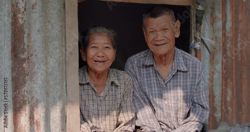 Happy smiling Asian woman and her husband who are poor elderly native farmer sitting on a narrow window. Used in humanity documentary concepts.