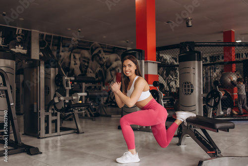 Pretty concentrated young sportswoman doing squats using bench in gym