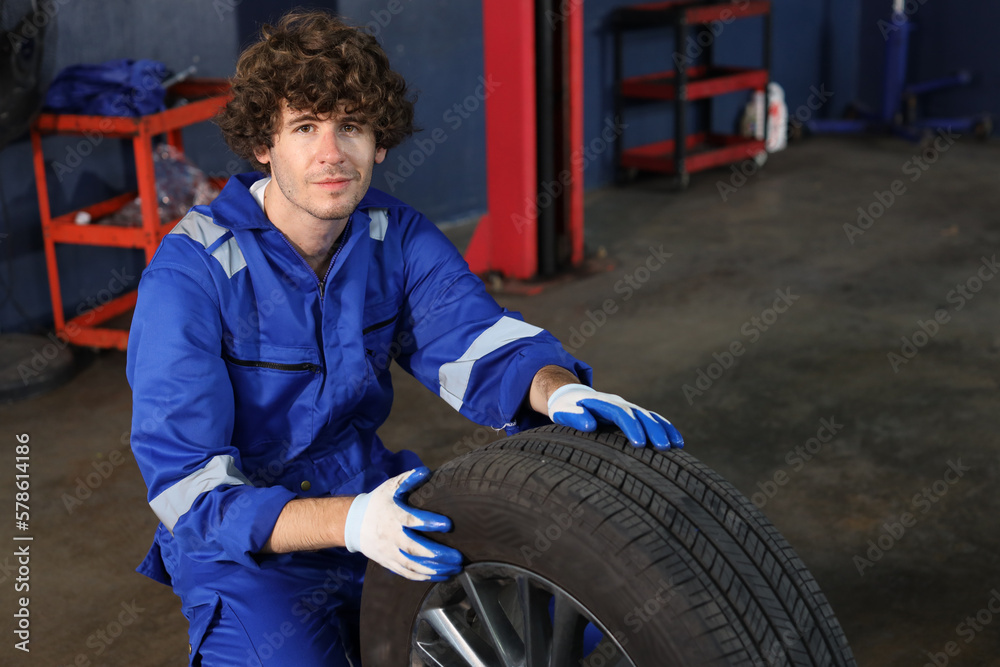 Man technician car mechanic in uniform holding tire for replacement or changeing at repair garage. Happy caucasian worker smiling and looking at camera. Concept of car center repair service. Man technician car mechanic in uniform holding tire for replacement or changeing at repair garage. Happy caucasian worker smiling and looking at camera. Concept of car center repair service.