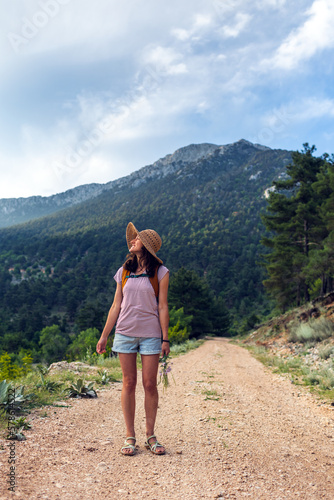 girl with a backpack enjoys the journey. the traveler stands on the road in the forest against the backdrop of mountains.