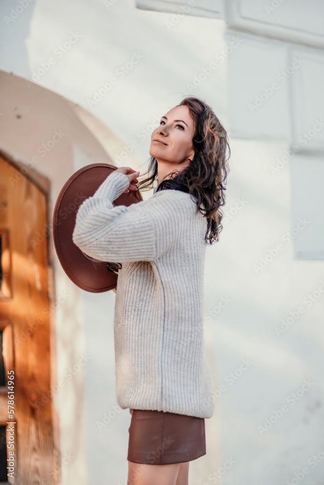 Woman walks in the city, lifestyle. Young beautiful woman in a loose light sweater, brown skirt and sneakers with a hat. Woman walks in the city, lifestyle. Young beautiful woman in a loose light sweater, brown skirt and sneakers with a hat.