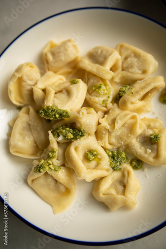ready hot ravioli with pesto sauce and grated cheese on a white plate close-up. dumplings ready to eat