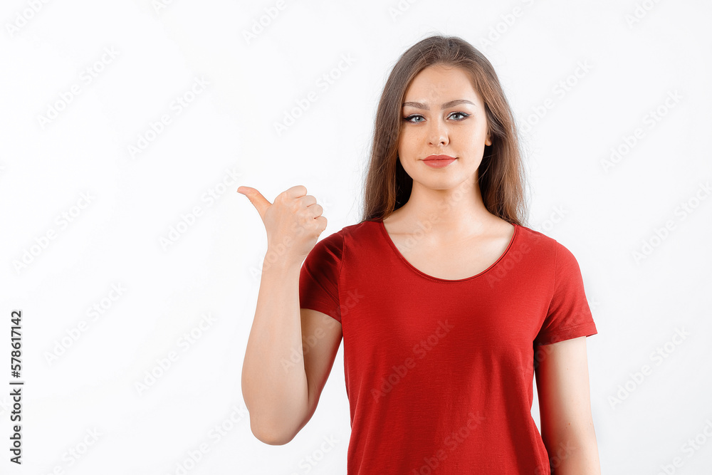 Happy lovely girl points finger at promo banner, shows advertisement on blank white space. Young brunette female stands over white background Happy lovely girl points finger at promo banner, shows advertisement on blank white space. Young brunette female stands over white background