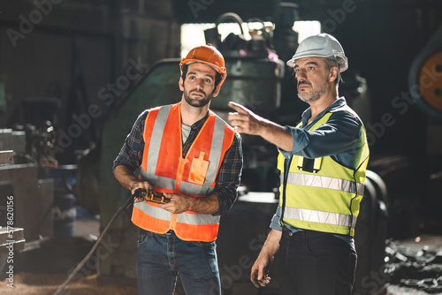 Fotografia, Obraz Senior male engineer training and explaining work to new employee wearing vest a