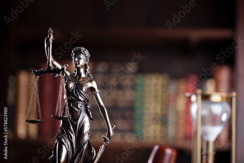 Judge chamber. Judge’s gavel, Themis sculpture, scale and legal books in the bookshelf.