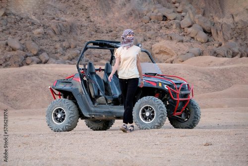 Young woman was riding a buggy. Walks away from him in the desert and looks away.