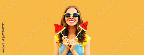 Summer portrait of happy smiling young woman with fresh juicy fruits, lollipop or ice cream shaped slice of watermelon on orange background