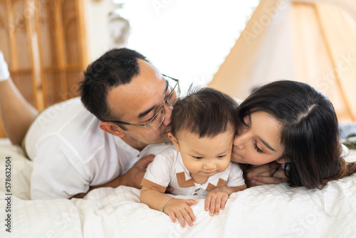 Portrait of enjoy happy love family asian father and mother playing with adorable little asian baby.dad touching with cute son moments good time in a white bedroom.Love of family concept