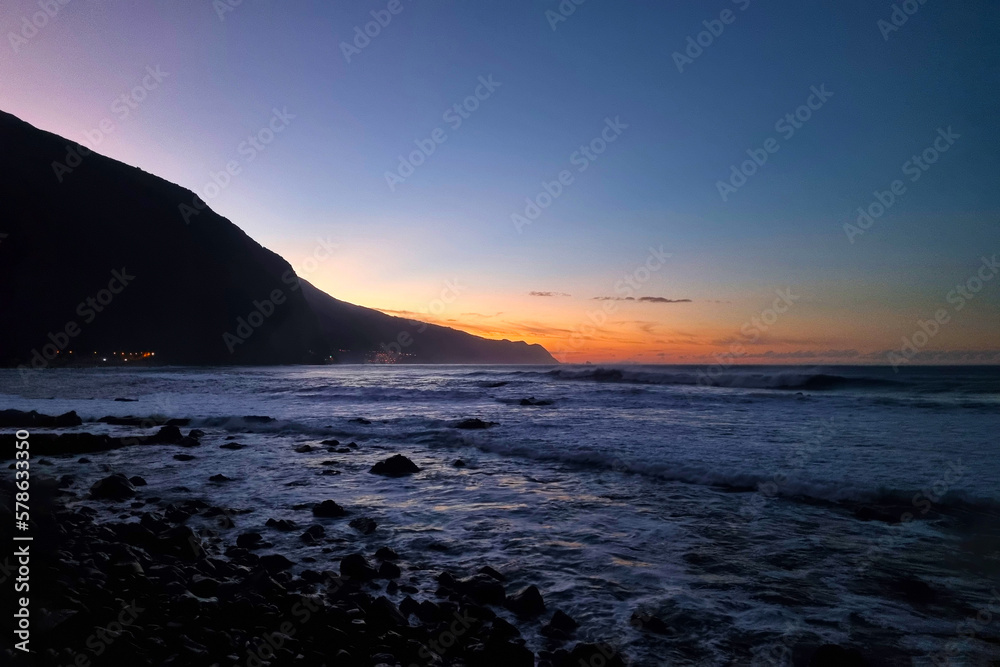 A picturesque sunset on the beach or ocean. Waves roll onto the beach. Rocky coast during sunset.