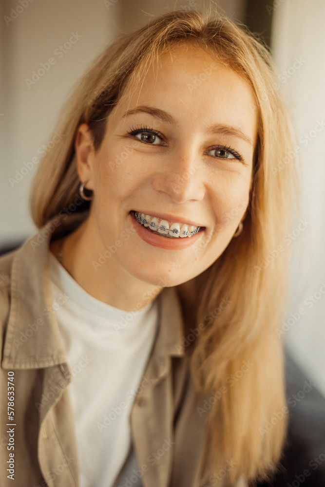Positive blonde female smiles in braces looking curiously at camera