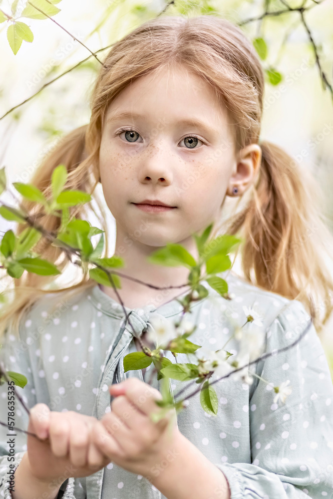 Close-up portrait of a toddler girl with red hair in front of a cherry blossom. Spring