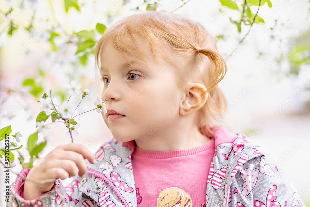 Close-up portrait of a toddler girl with red hair in front of a cherry blossom. Spring Close-up portrait of a toddler girl with red hair in front of a cherry blossom. Spring