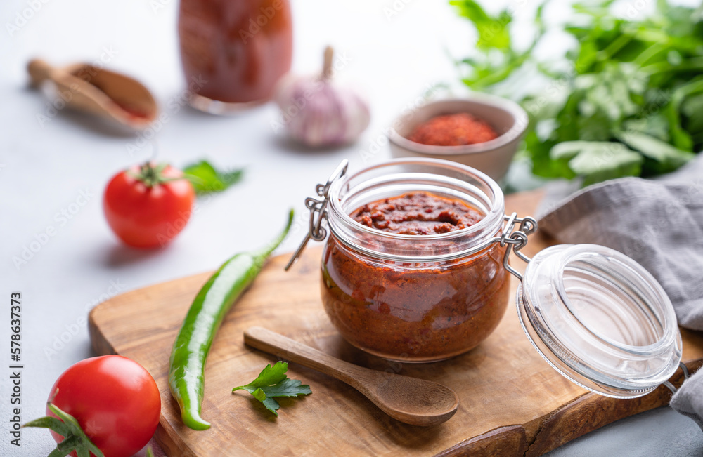 Homemade tomato sauce for pizza or pasta in a jar on a light background with fresh vegetables and herbs close up.