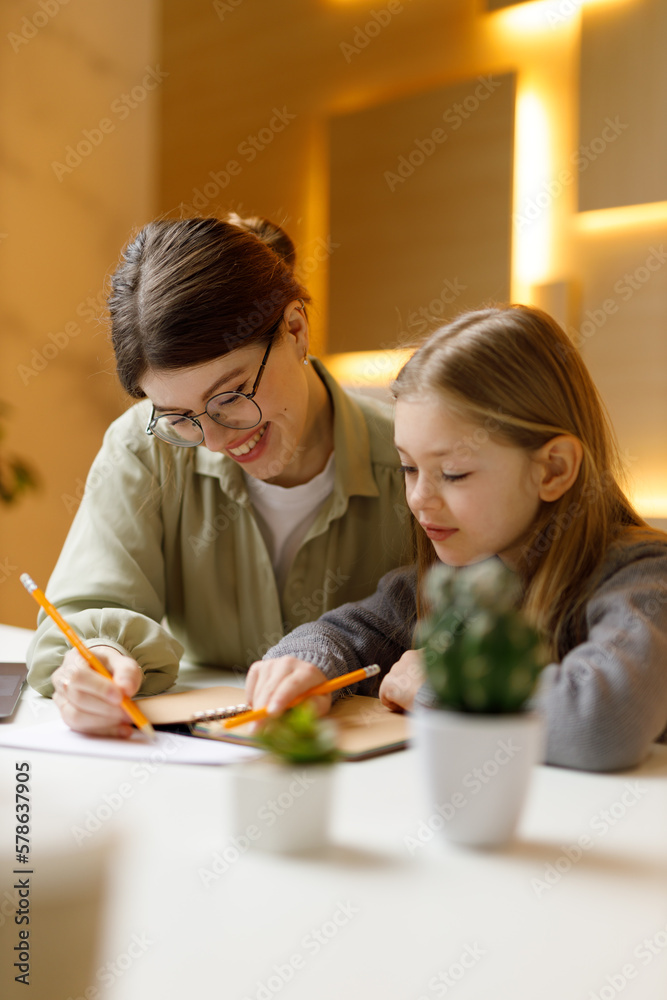 The teacher explains the lesson to the little girl, mother and child write in a notebook and smile. The teacher explains the lesson to the little girl, mother and child write in a notebook and smile.