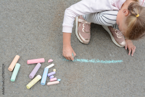 Little child drawing happy family with chalk on asphalt, above view