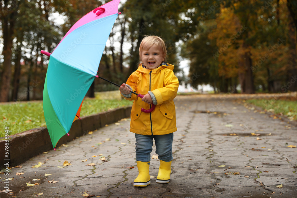 Φωτογραφία Little girl holding colorful umbrella and walking near puddles outdoors