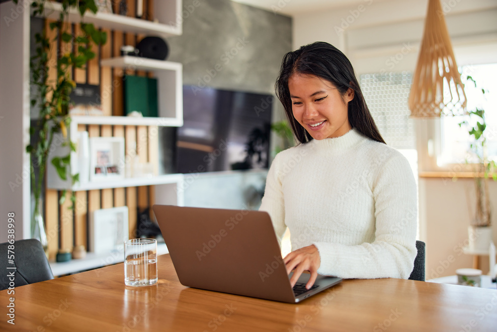 A smiling Asian woman working over the laptop, sitting at the home office. A smiling Asian woman working over the laptop, sitting at the home office.
