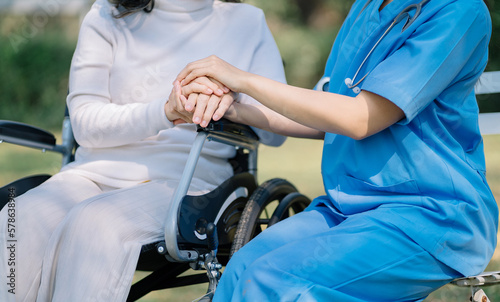 Happy patient is holding caregiver for a hand while spending time together outdoor.