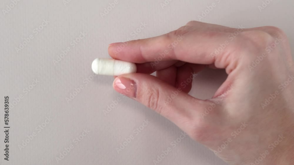 A large white capsule with a supplement in a woman's hand against a white background. Pills, medicines and vitamins. A large white capsule with a supplement in a woman's hand against a white background. Pills, medicines and vitamins.