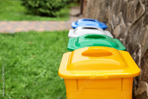 Many colorful recycling bins near stone wall outdoors, closeup. Space for text