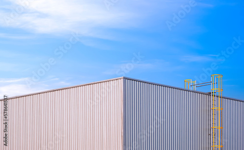Symmetric view of white Corrugated iron Industrial Building with yellow cylinder Ladder against blue sky Background
