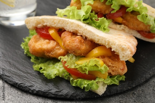 Delicious pita sandwiches with fried fish, pepper, tomatoes and lettuce on dark grey table, closeup