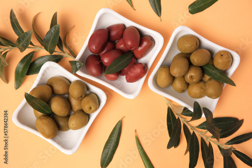 Different fresh olives and green leaves on pale orange background, flat lay