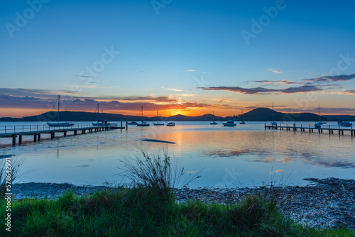 Sunrise waterscape with boats, wharves and sun coming over the mountain range