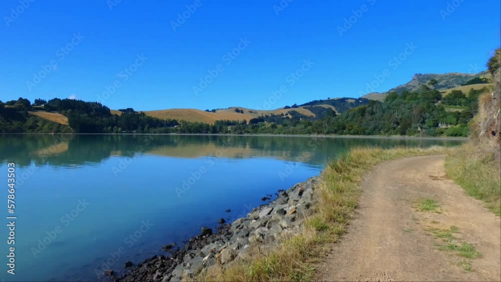 Walking on coastal track in harbor with nice reflection of low hills on calm water - Governors Bay Track, Banks Peninsula (New Zealand) Walking on coastal track in harbor with nice reflection of low hills on calm water - Governors Bay Track, Banks Peninsula (New Zealand)