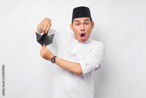 Surprised young Asian Muslim man in Arabic clothes showing empty wallet and looking at camera isolated on white background. People religious Islamic lifestyle concept