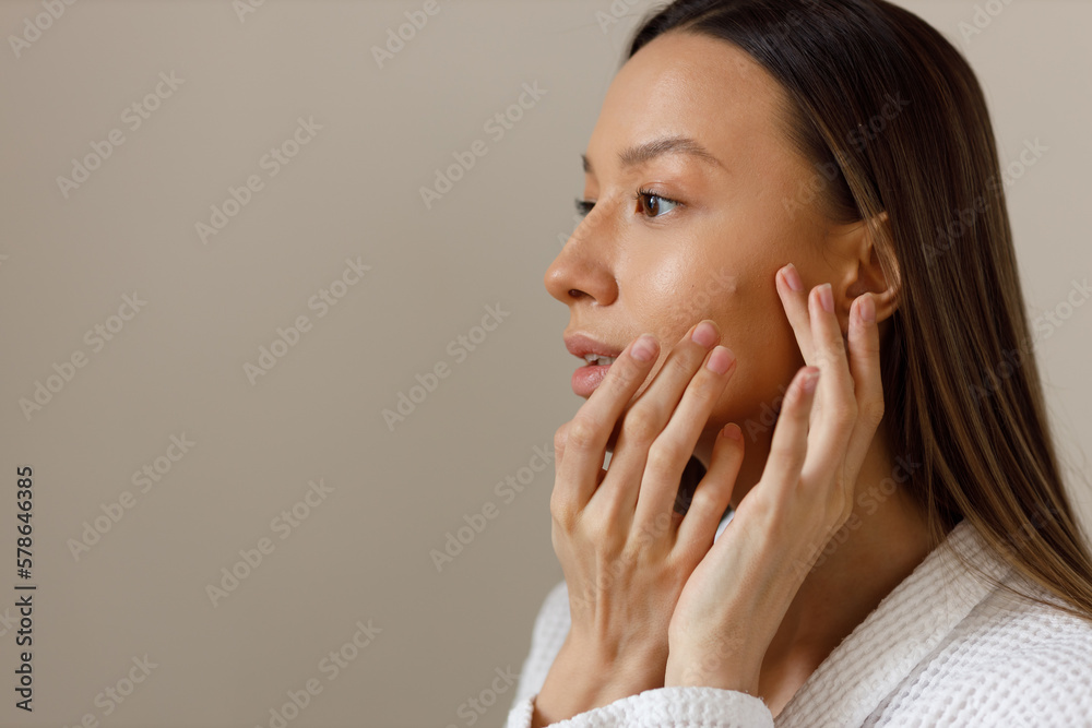 Acne skin of young woman in white bathrobe examines pimples on her face. Problematic skin on the face pustula. Portrait of girl removing pimples in the bathroom. Beauty and health of the skin. - obrazy, fototapety, plakaty 