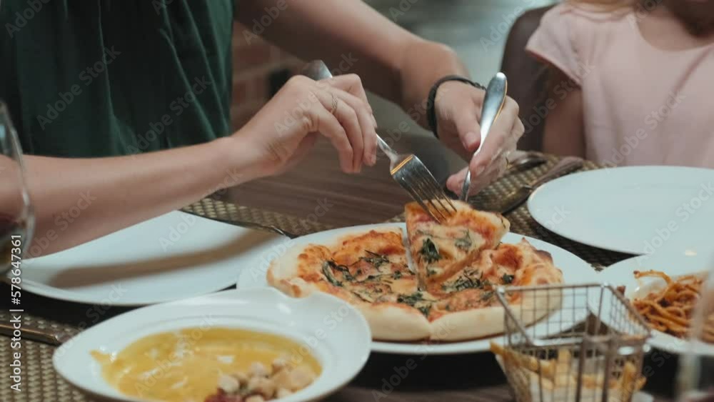 Tilt down shot of mother serving slice of pizza on plate for little daughter while having family dinner in restaurant Tilt down shot of mother serving slice of pizza on plate for little daughter while having family dinner in restaurant