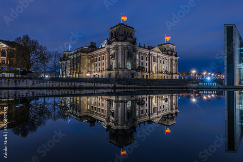 Blue hour in the government district of Berlin. Reichstag in the capital of Germany. River Spree in the city center with reflection from the building. Illuminated building on a winter evening