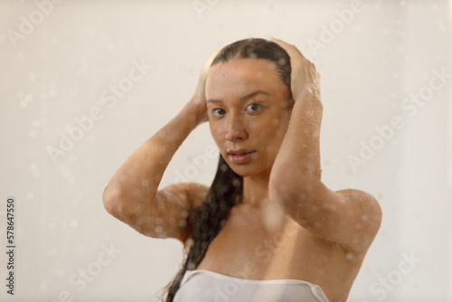 Young woman under the trickles of water in pleasure shower. Beautiful girl under the spray of water. Wet through glass drops selective focus