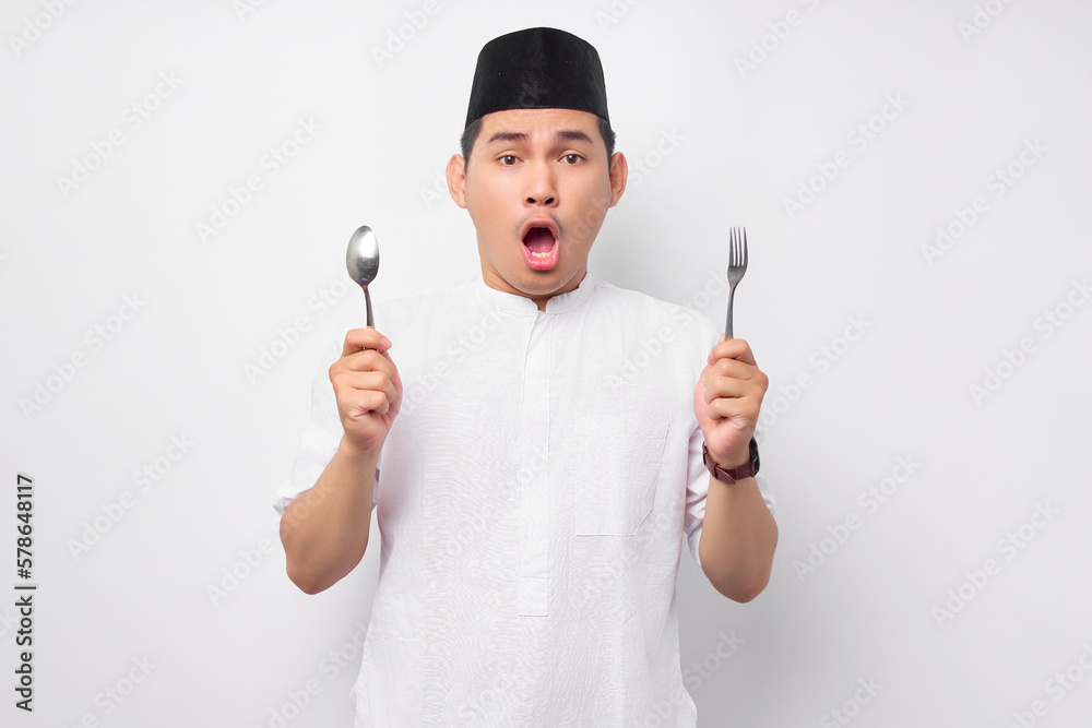 Surprised young Asian Muslim man in Arabic clothes holding spoon and