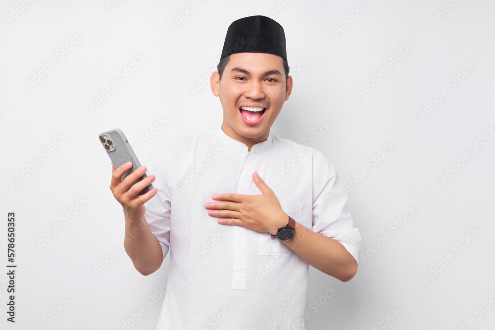 Smiling happy handsome young Asian Muslim man in Arabic clothes holding mobile phone and receiving good news isolated on white background. People religious Islamic lifestyle concept Smiling happy handsome young Asian Muslim man in Arabic clothes holding mobile phone and receiving good news isolated on white background. People religious Islamic lifestyle concept