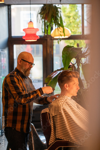 Bearded male barber cutting hair of a client in a barbershop. High quality photo