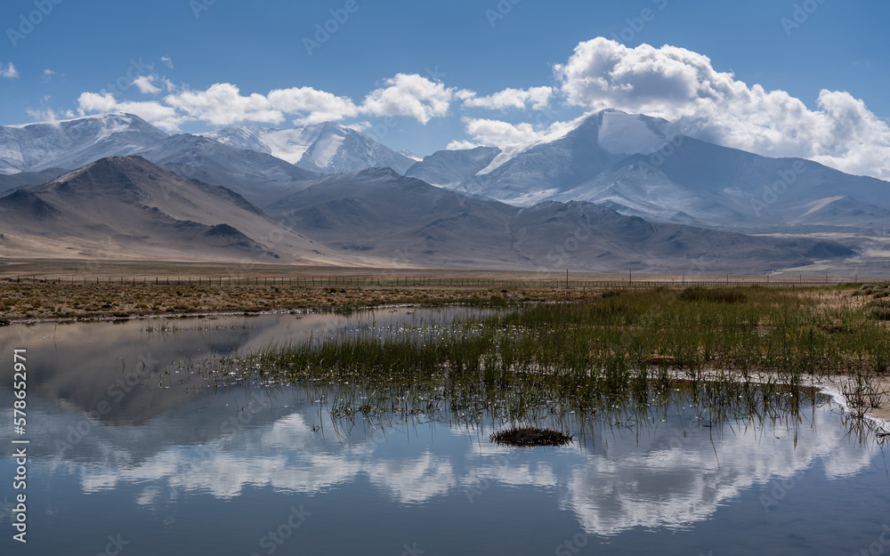 Scenic high altitude mountain landscape with blue sky and clouds reflection in water near Karakul lake on Pamir Highway, Murghab, Gorno-Badakshan, Tajikistan